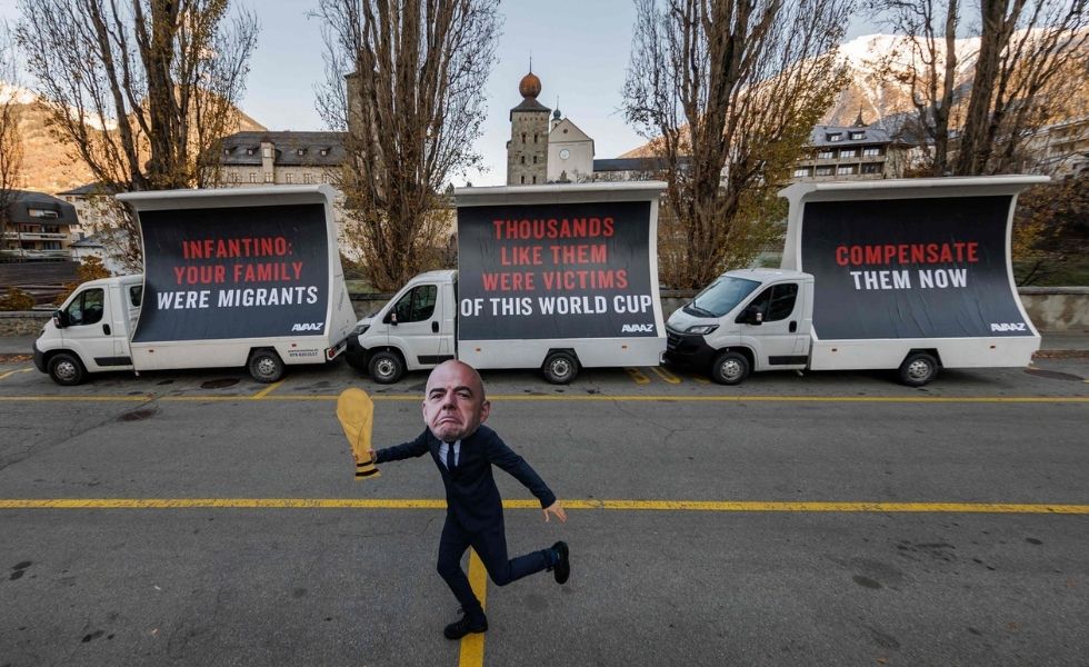 A man with a mask representing FIFA President Gianni Infantino and a football World Cup trophee gestures next to giant billboards in a street of Infantino's hometown of Brig, where his parents originally moved as migrants, during a protest by NGO Avaaz calling on Infantino to commit to a $440 million FIFA compensation fund for victims of this Qatar 2022 World Cup football tournament, on December 7, 2022. 
